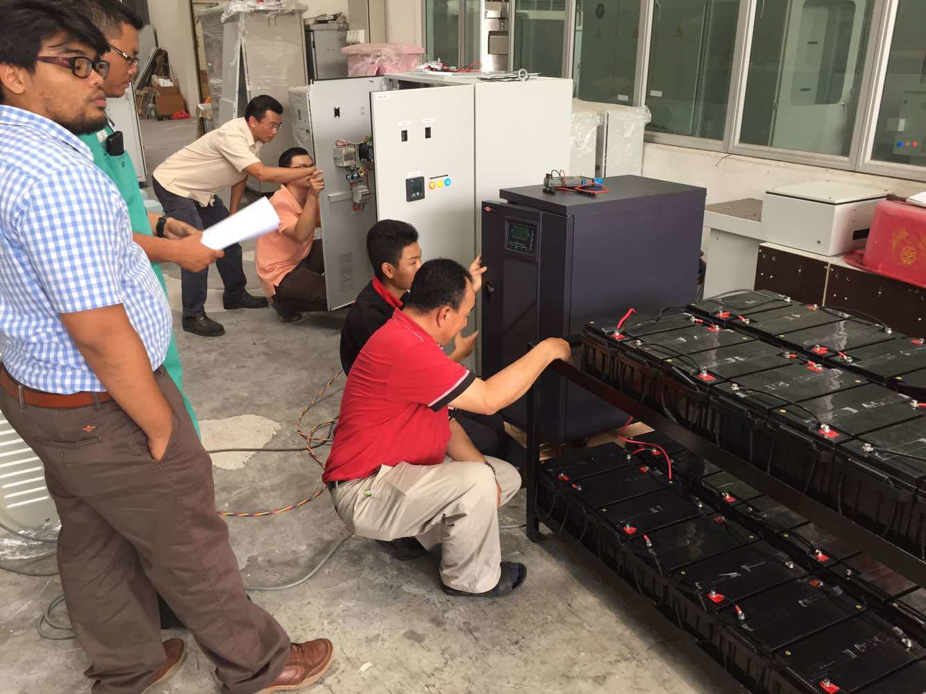 Group of men installing equipment; batteries in foreground, electrical panels in background.