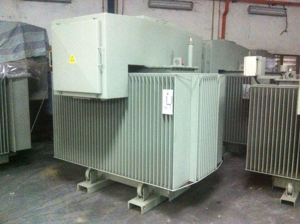 Large electrical transformer, metal with cooling fins, in a warehouse setting.
