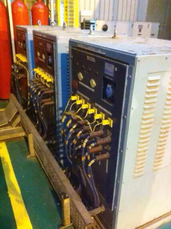 Three large industrial electrical units, blue and gray, with many wires and gauges, inside a building.