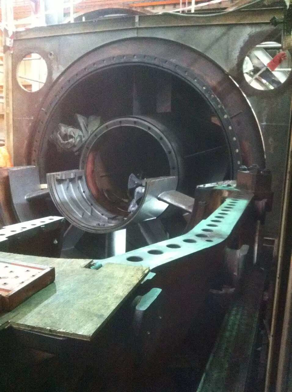 Large industrial machine with open cylindrical chamber holding a metal component. Dark setting, possible factory.