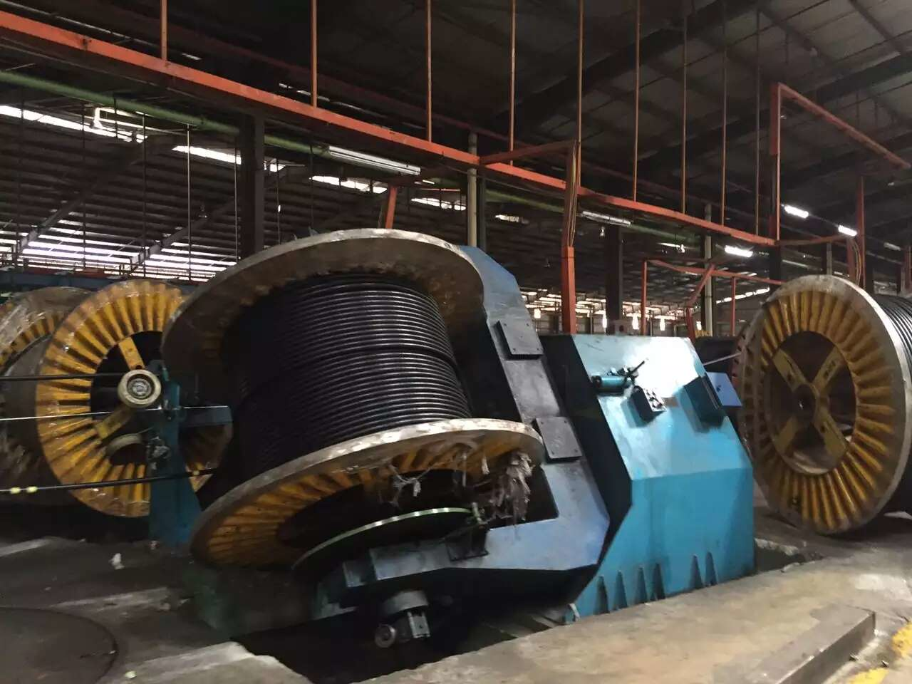 Large spool of black cable on a machine in a factory, with other cable spools visible.