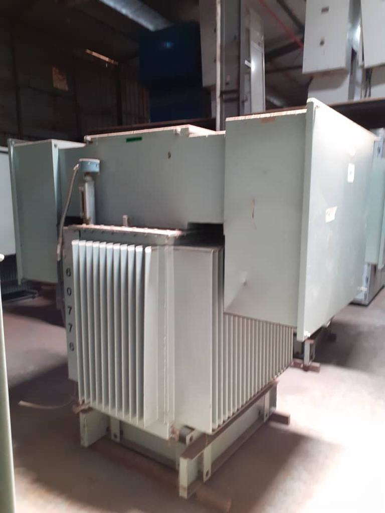 Large, industrial transformer with gray cooling fins and a beige cabinet, in a warehouse setting.