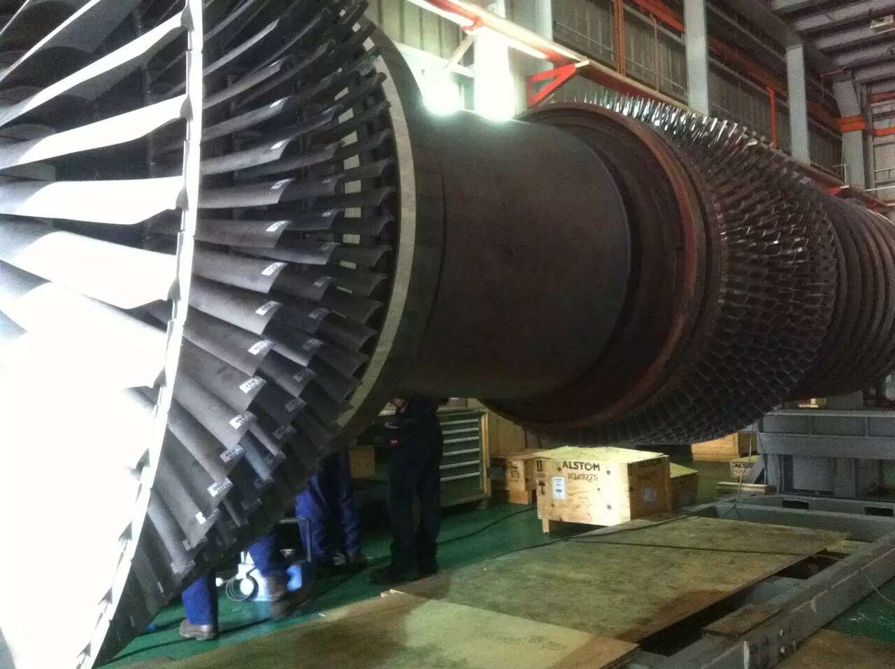 Large turbine rotor being inspected by workers in a factory setting.