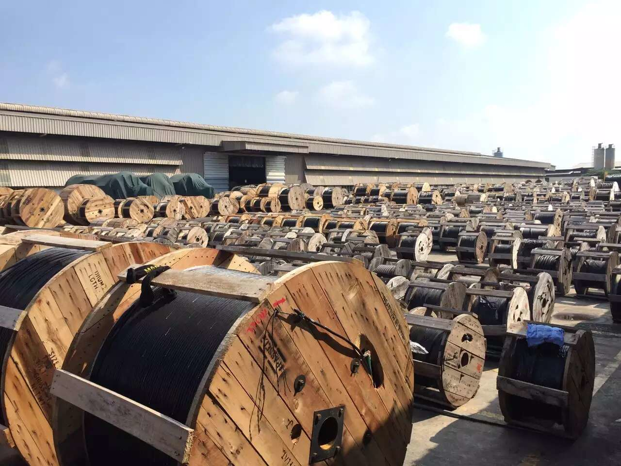 Wooden cable spools outside a warehouse under a sunny sky.