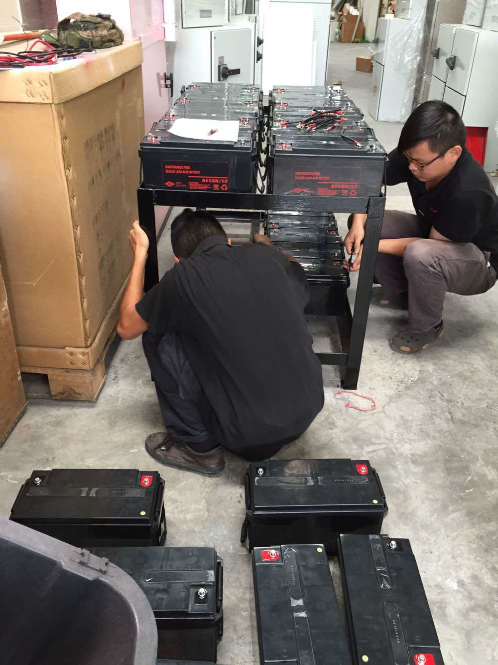 Two men installing batteries on a rack inside a warehouse.