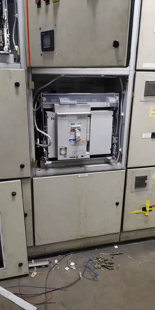 Electrical panel with open access door. Wires, electrical components visible. Beige and gray colors. Industrial setting.