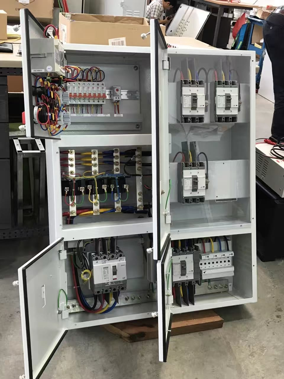 Opened electrical cabinet with wires, circuit breakers, and terminals. White, indoor.