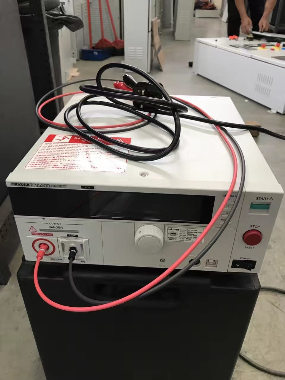 White power supply unit with attached cables on a black box; red and black wires.