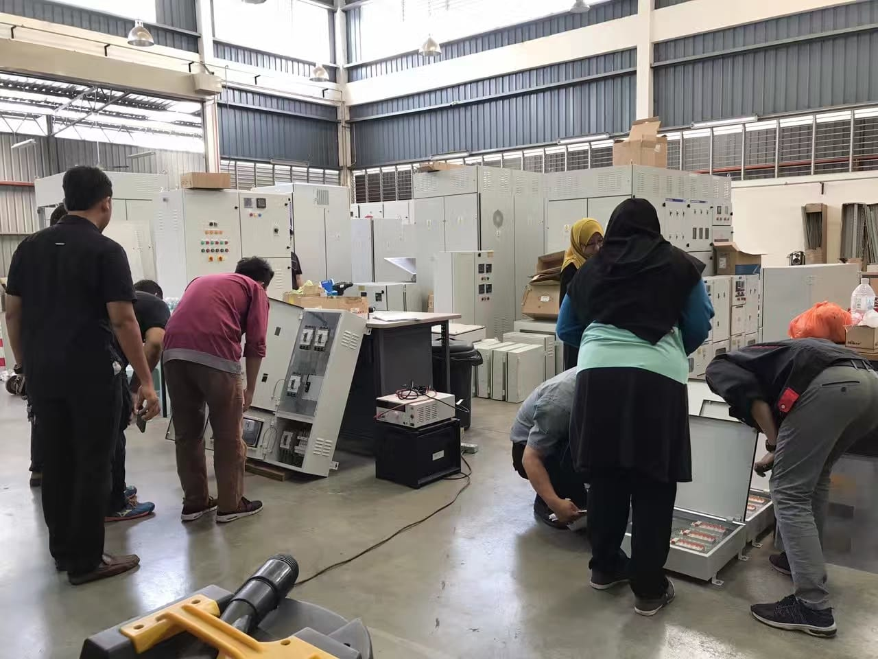 People working on electrical panels in a large warehouse.