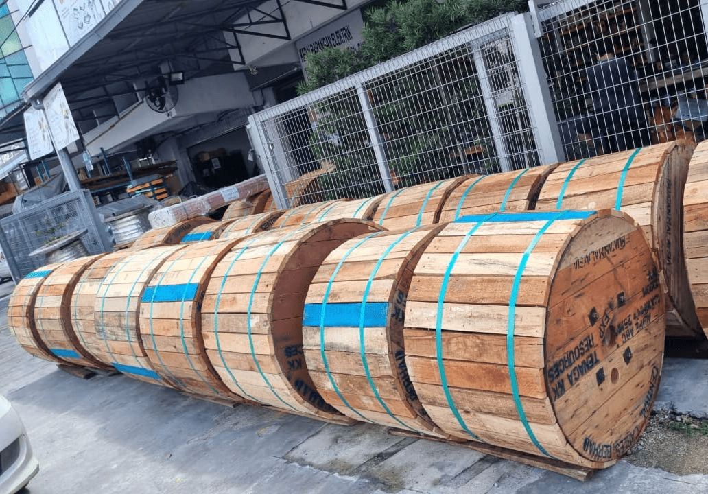 Wooden spools of cable, bound with blue straps, sit outdoors.