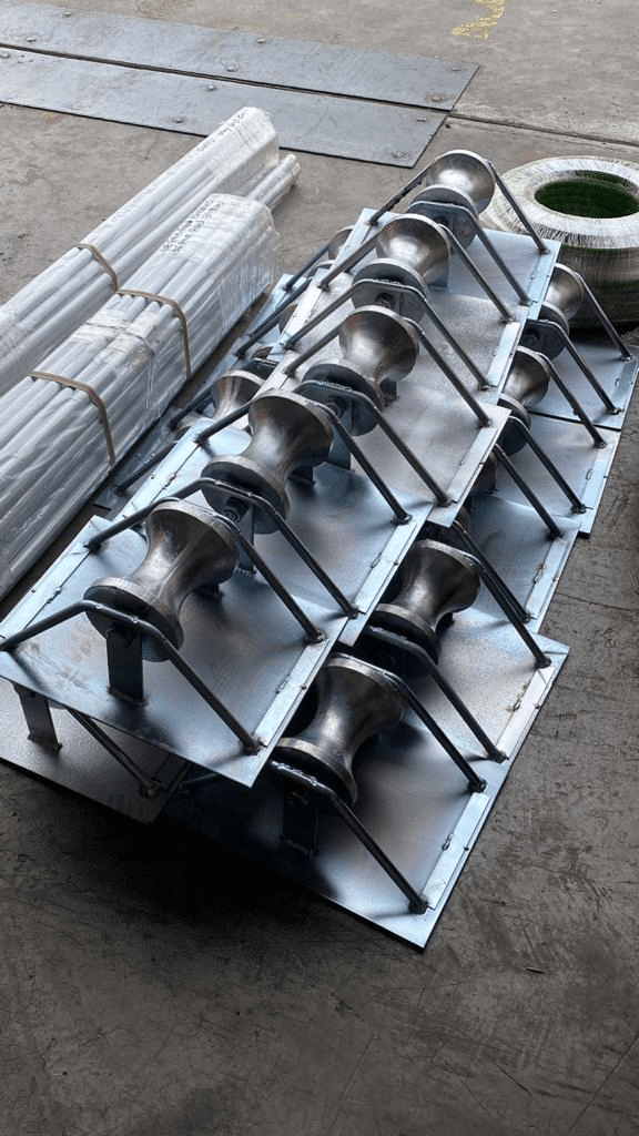 Metal rollers on steel plates, bundled pipes, and a green-rimmed cylinder on a gray surface.