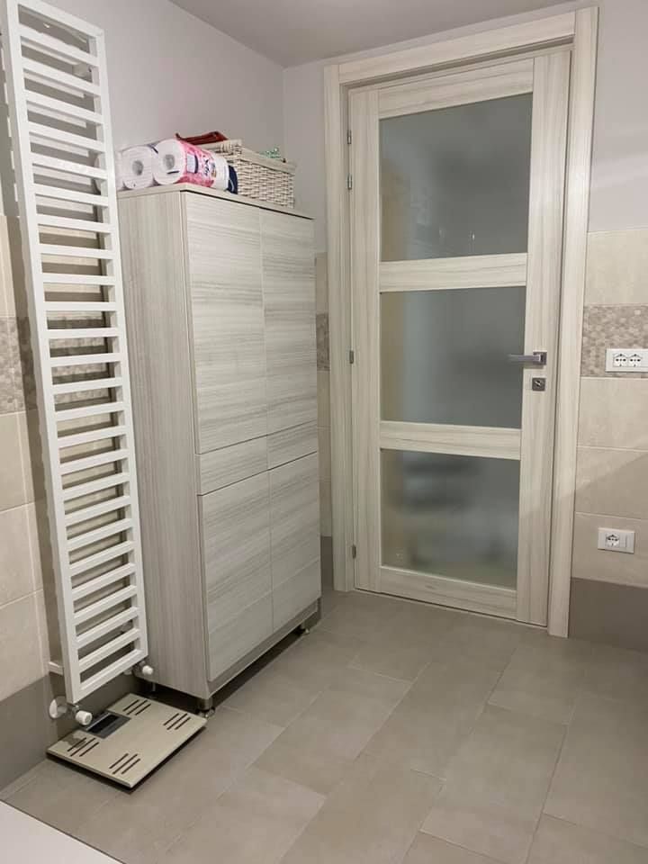 Bagno con portasciugamani bianco, mobiletto, porta in vetro smerigliato e bilancia sul pavimento.
