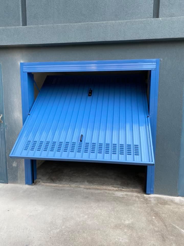 Porta del garage blu, parzialmente aperta, incassata in una parete grigia.