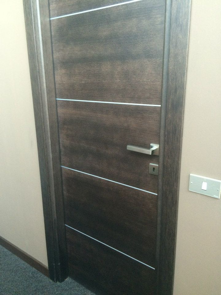 Porta marrone scuro con strisce e maniglia argentate; parete beige.