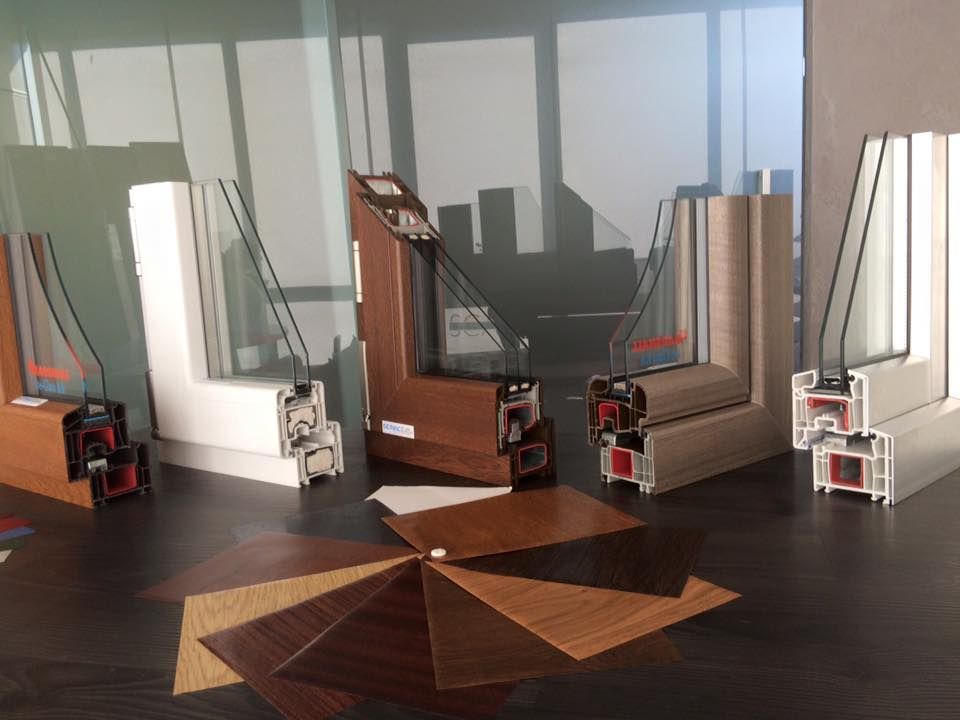 Sezioni trasversali di telai di finestre in vari colori, esposte con campioni di legno su un tavolo.