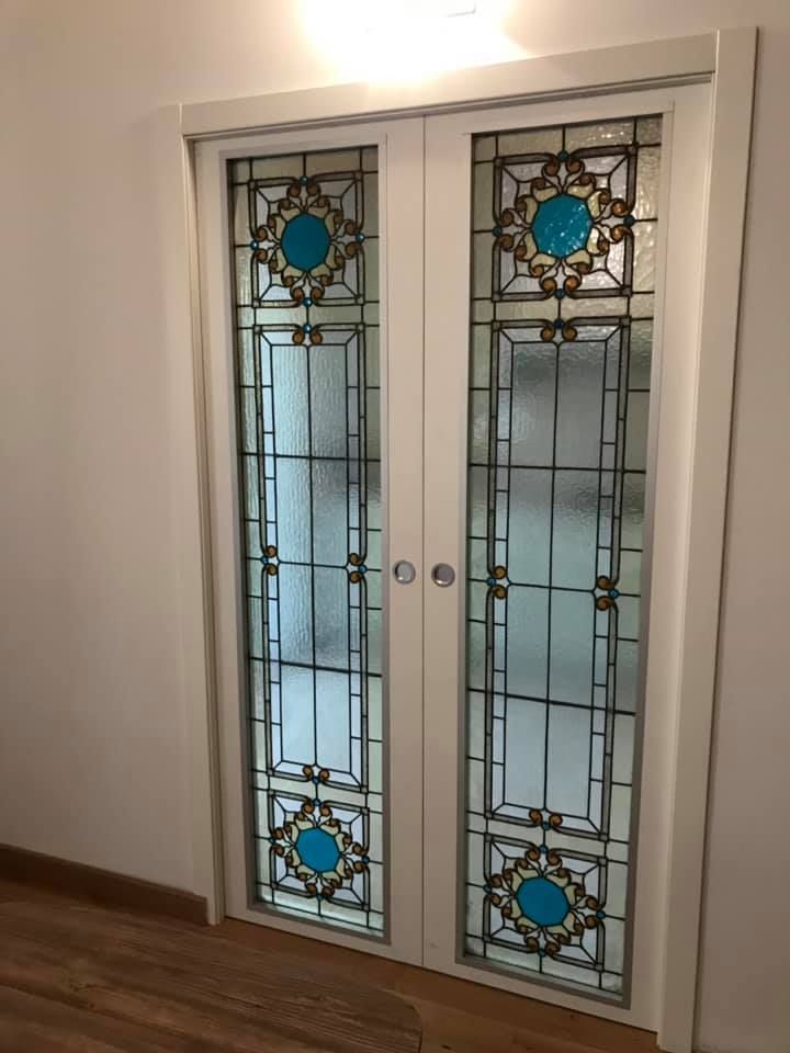 Coppia di porte in vetro con cornice bianca e pannelli decorativi in vetro colorato con accenti color verde acqua e oro.