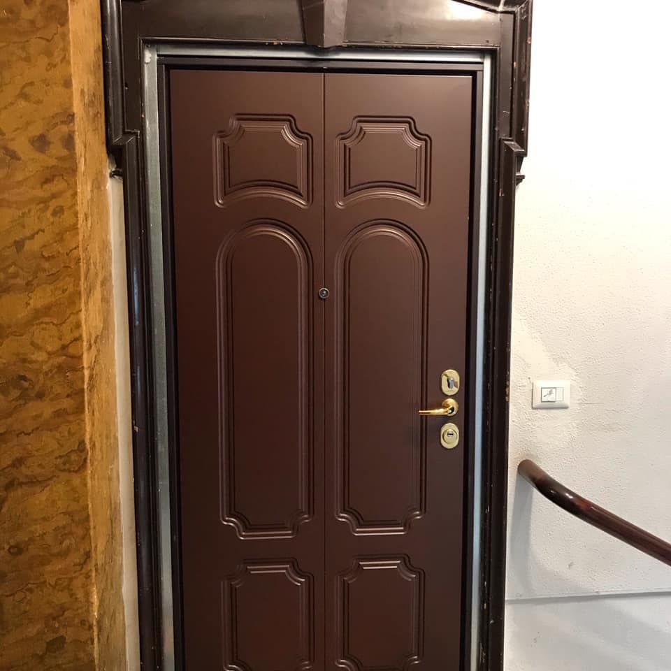 Porta doppia marrone con pannelli decorativi e ferramenta dorata, in un corridoio.