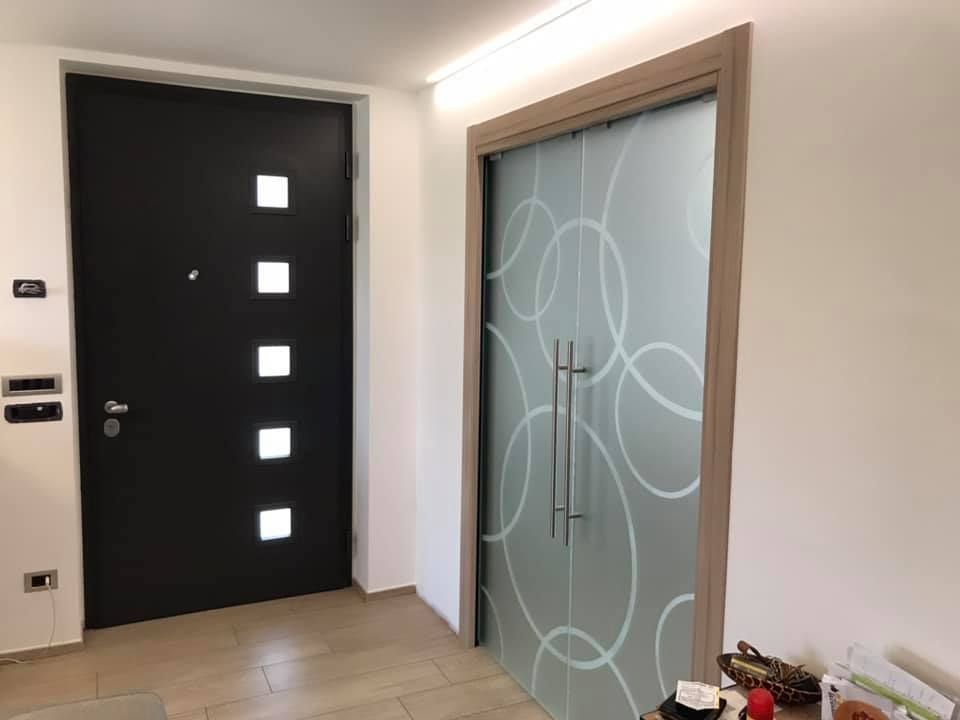 Porta nera con finestre quadrate accanto a una porta in vetro smerigliato con un motivo a cerchi bianchi.