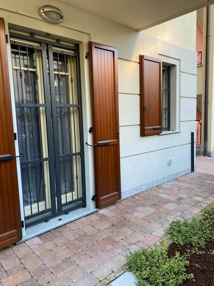 Esterno dell'edificio con persiane marroni e porta di sicurezza in metallo, su un patio in mattoni.