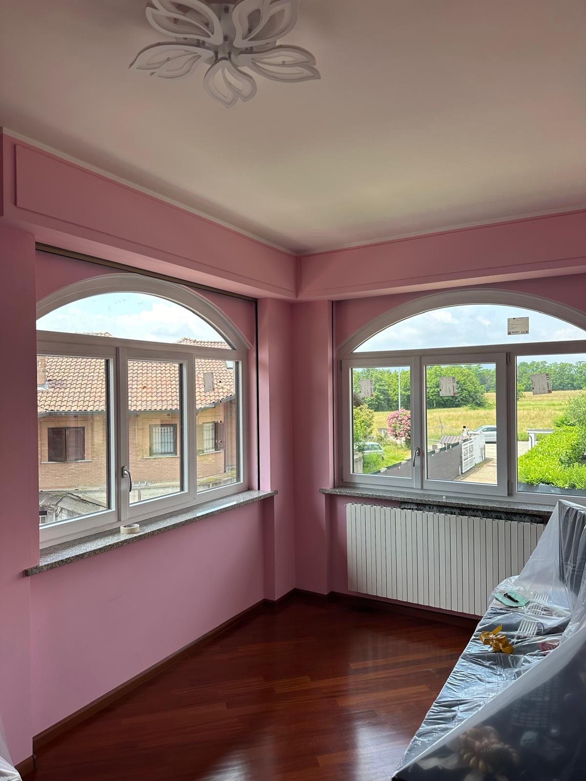 Camera dipinta di rosa con finestre ad arco, pavimenti in legno e lampadario a soffitto. Vista sul paesaggio urbano esterno.