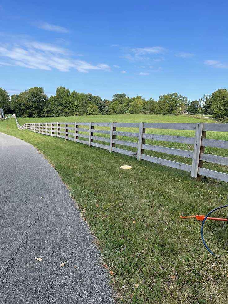Wooden fence along a grassy field on a sunny day.