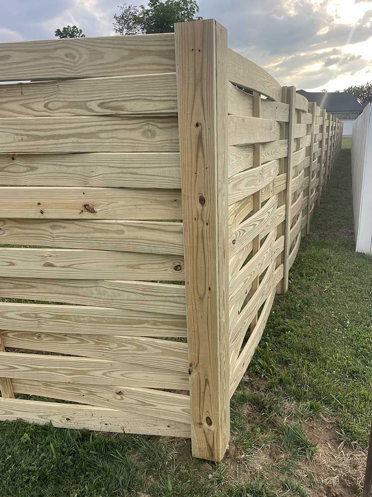 Wooden fence with horizontal boards, outdoors on a grassy area, overcast sky.