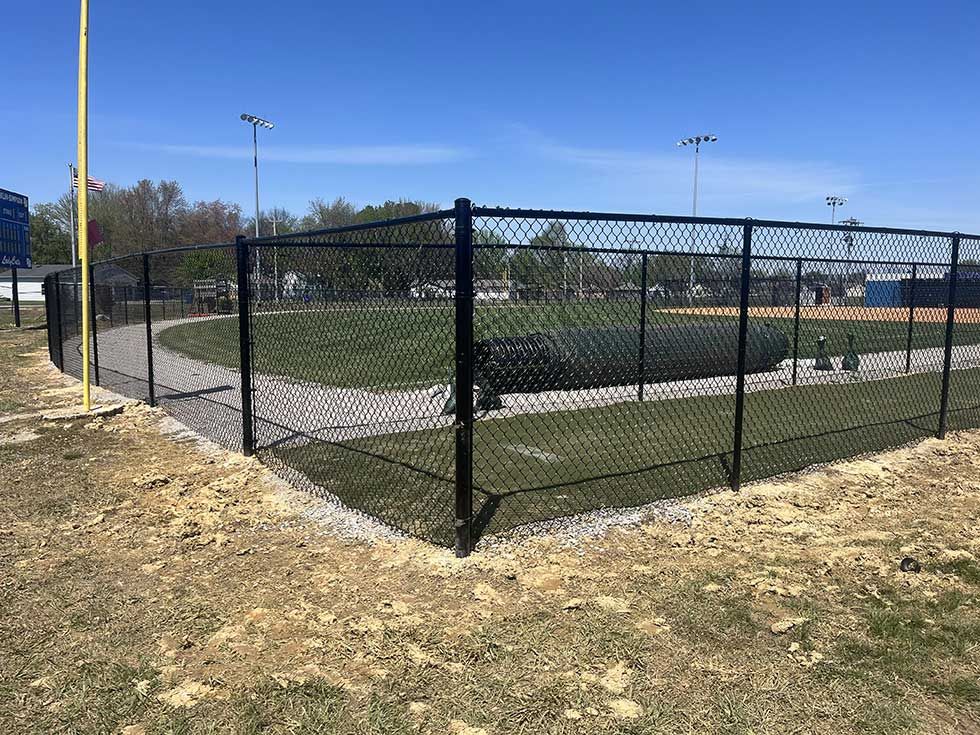 Baseball field enclosed by a black chain-link fence on a sunny day.