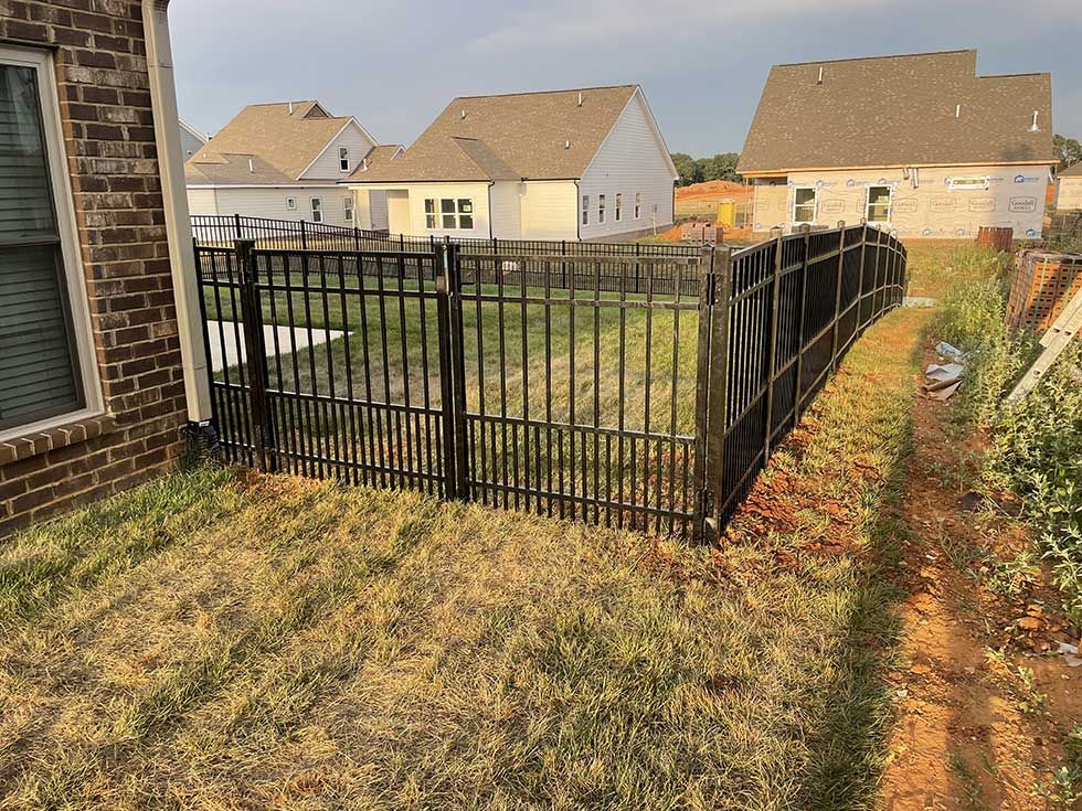 Black metal fence in backyard, enclosing a grassy area. Houses in background.