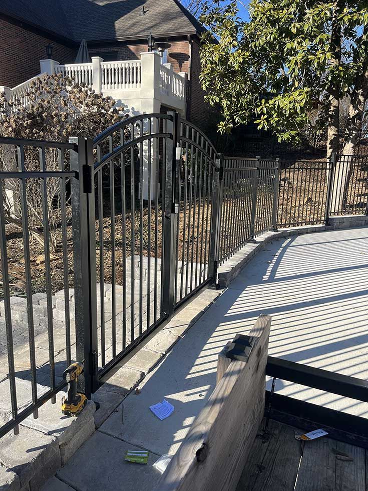 Black metal fence surrounds a concrete patio near a house with a white balcony.