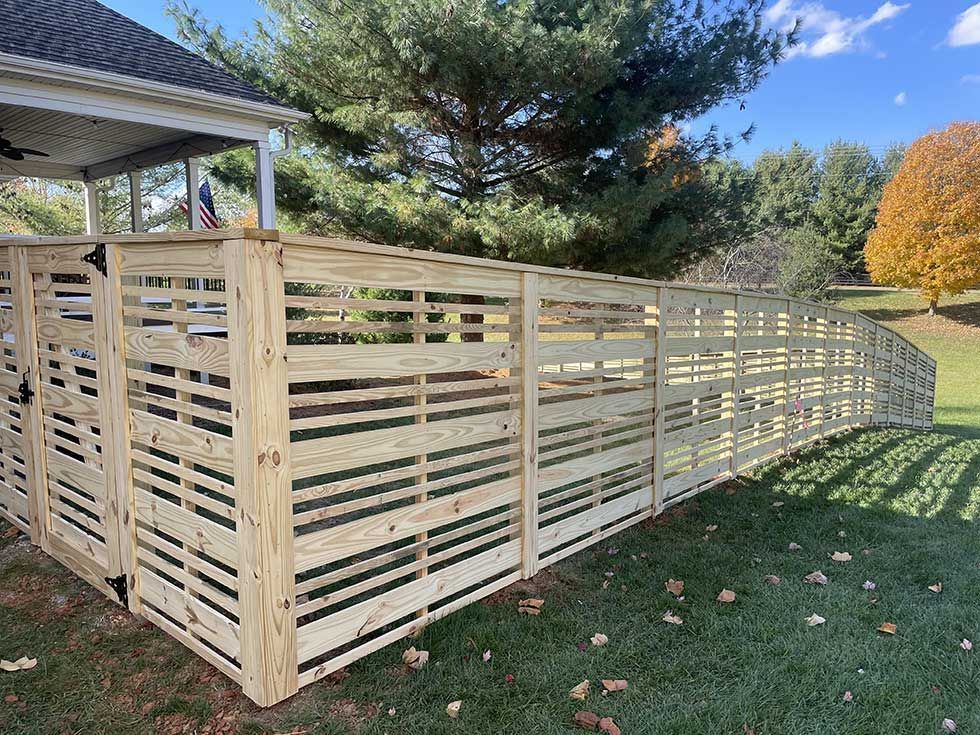 Wooden horizontal slat fence curves around a yard, next to a house with a porch.