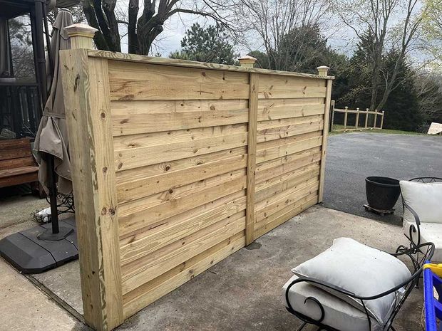 Wooden fence on a concrete patio, with outdoor furniture and a trash can.
