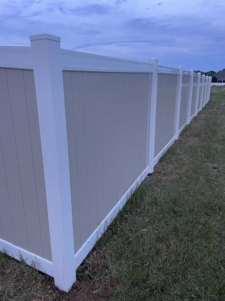 Beige and white vinyl fence in a grassy yard under a cloudy sky.