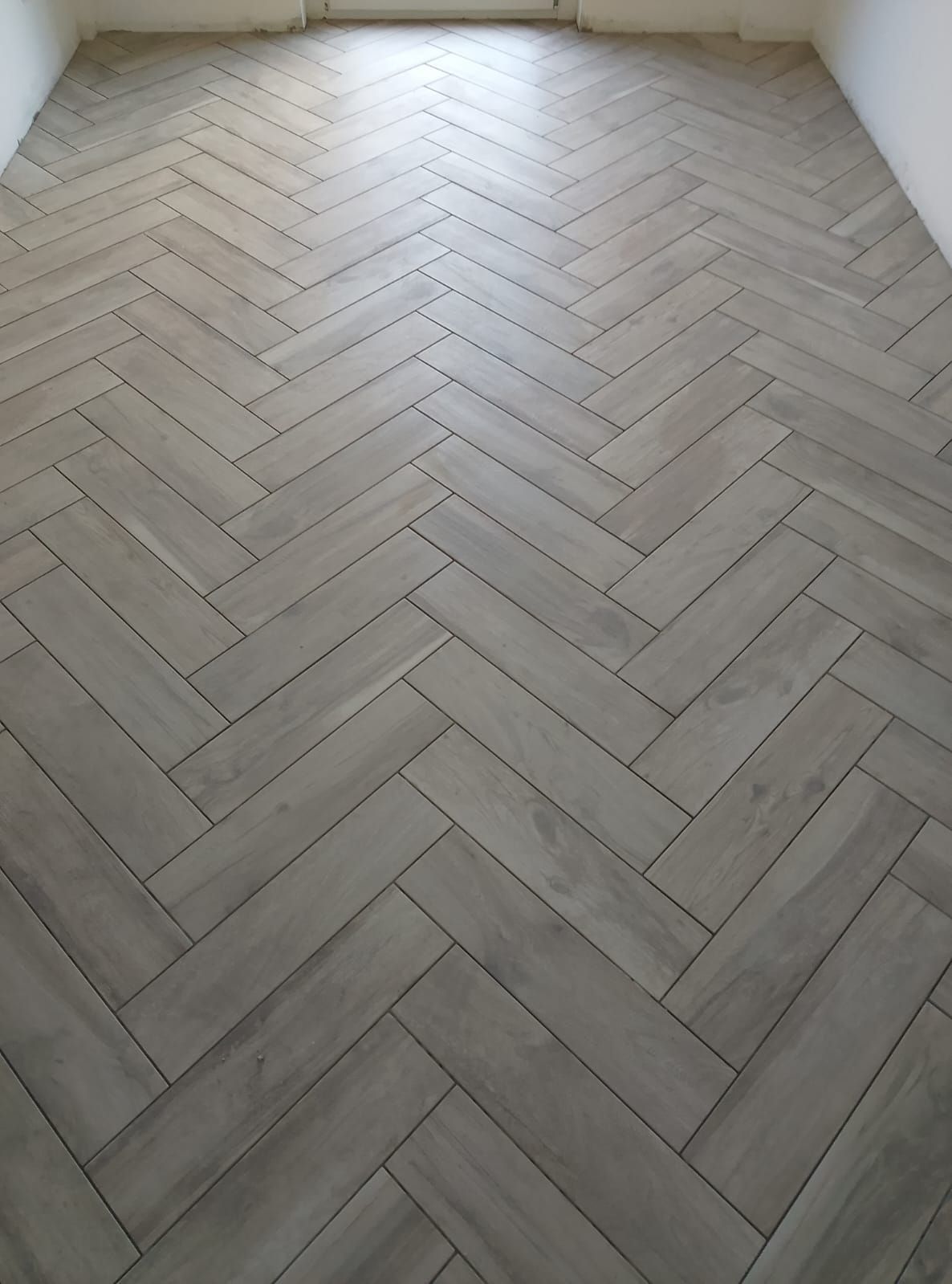 Listoni grigio chiaro effetto legno posati secondo il classico schema a spina di pesce rivestono il pavimento di una stanza.