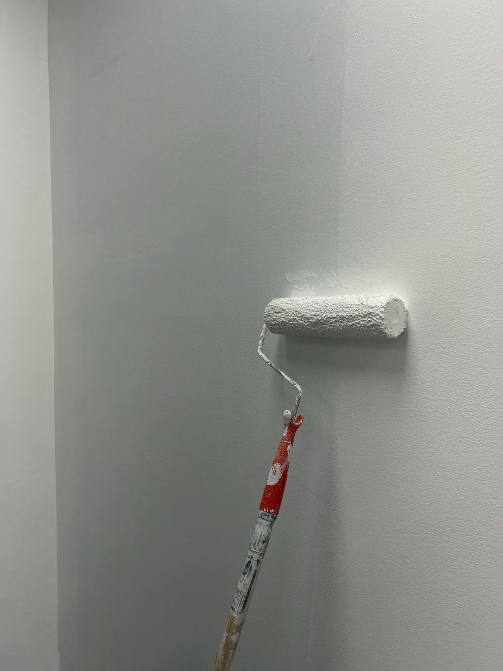 Un rullo da pittura con manicotto bianco che dipinge una parete grigio chiaro.