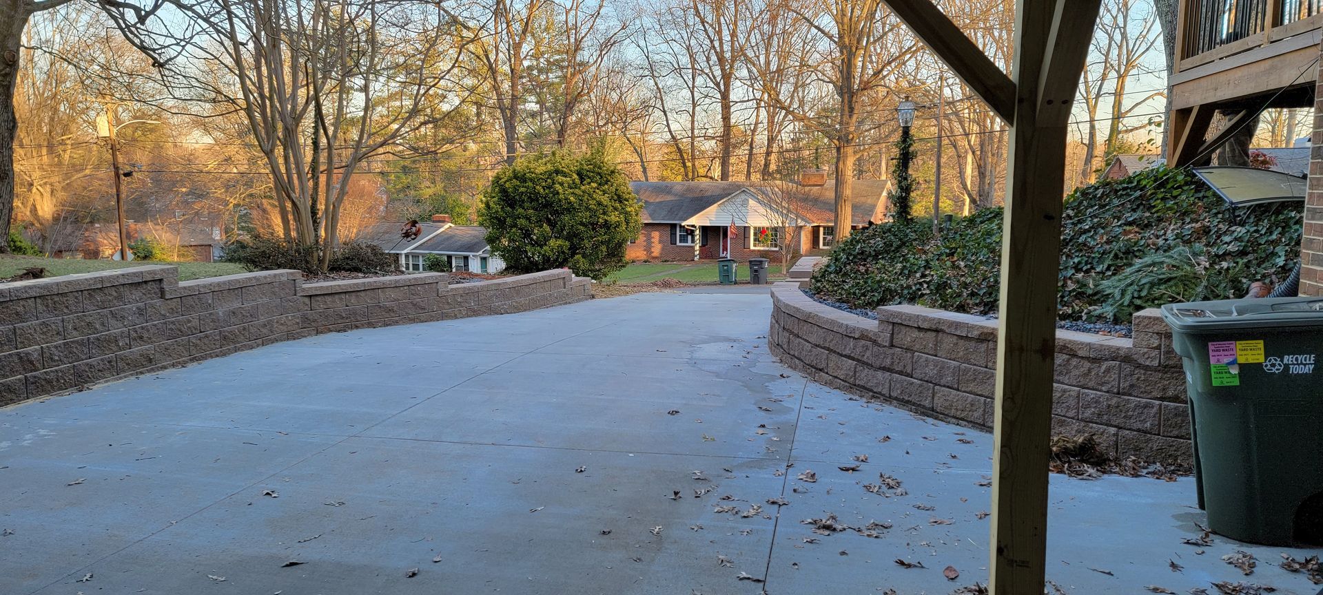 A driveway leading to a house with a green trash can in the foreground.