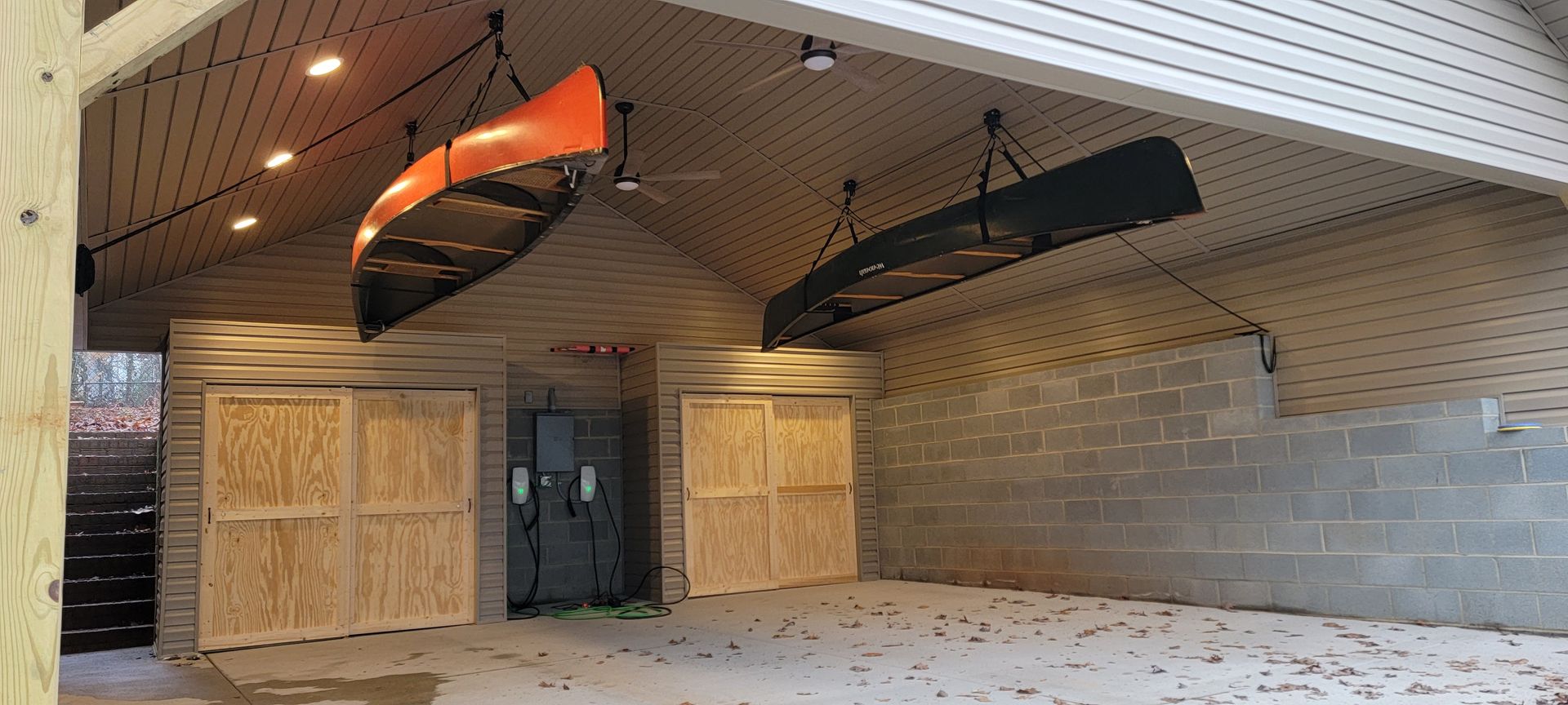 Two kayaks are hanging from the ceiling of a garage.