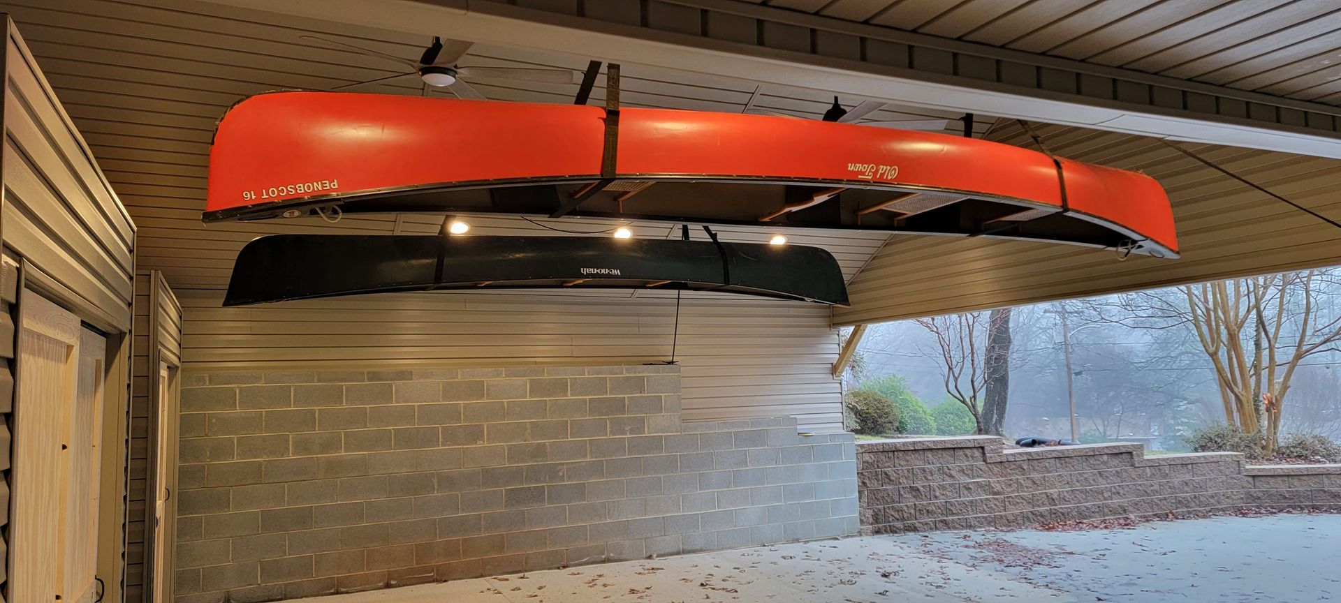 A red canoe is hanging from the ceiling of a garage.