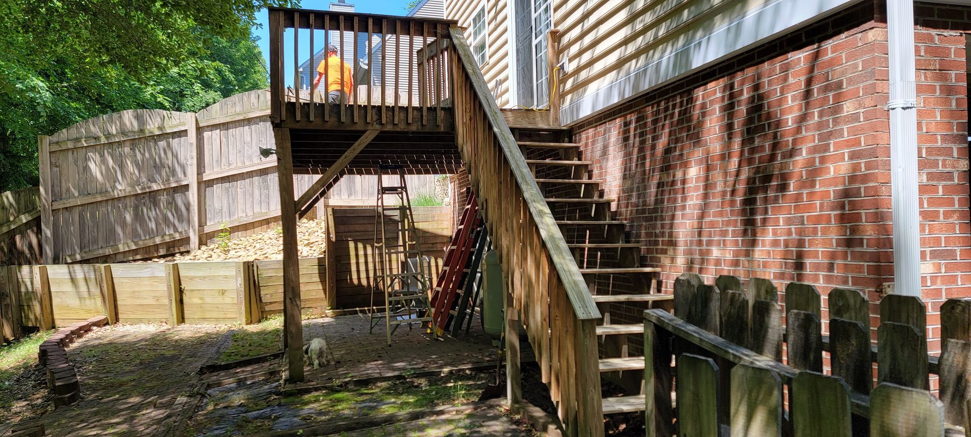 A wooden deck with stairs leading up to it is in the backyard of a house.