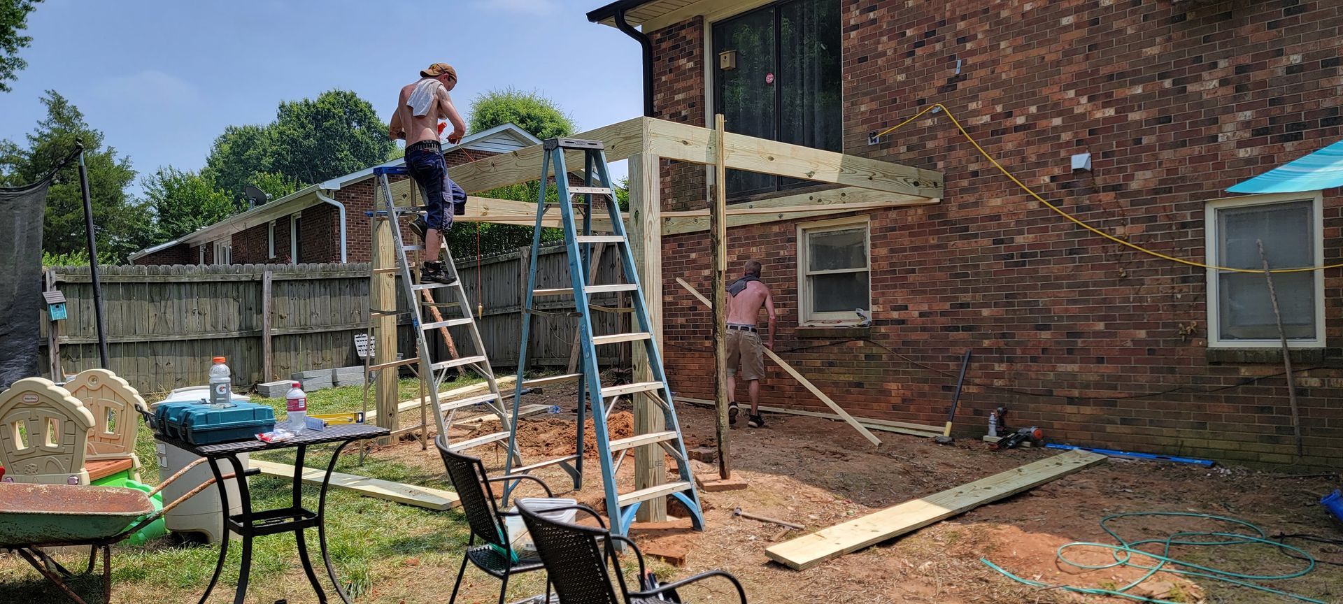 A man is standing on a ladder in front of a brick house.