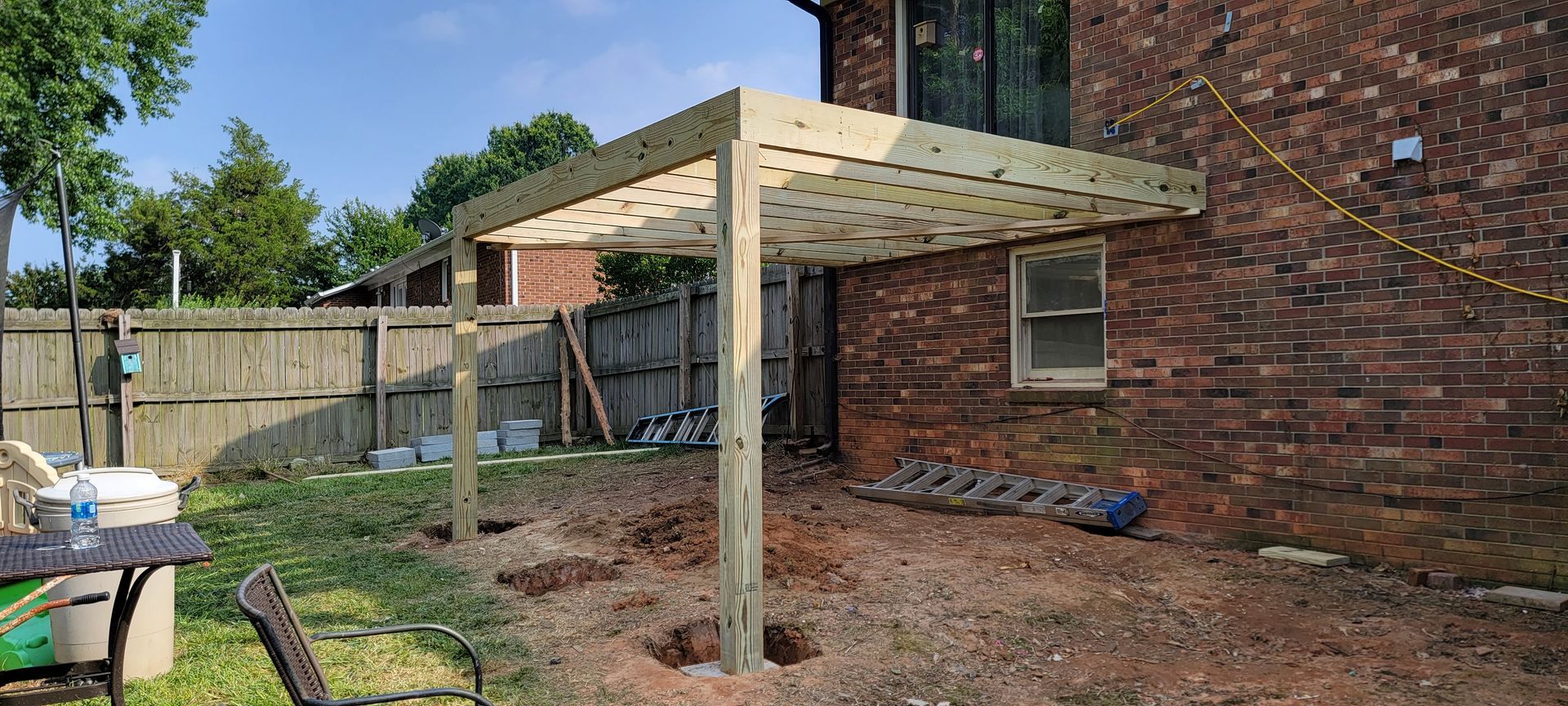 A wooden deck is being built in the backyard of a brick house.