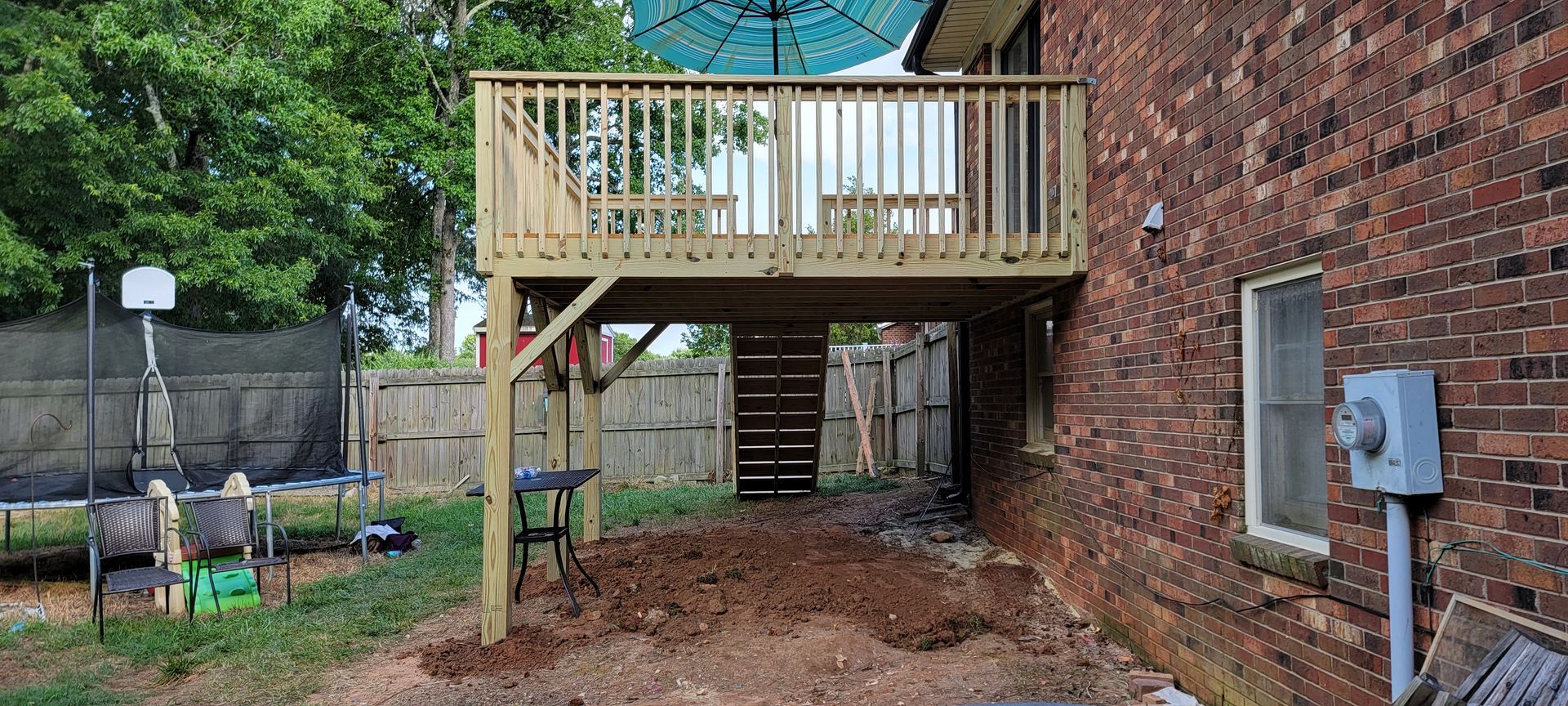 A wooden deck is being built in the backyard of a brick house.