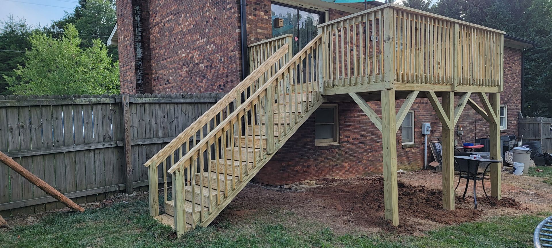 A wooden deck with stairs leading up to it in front of a brick house.