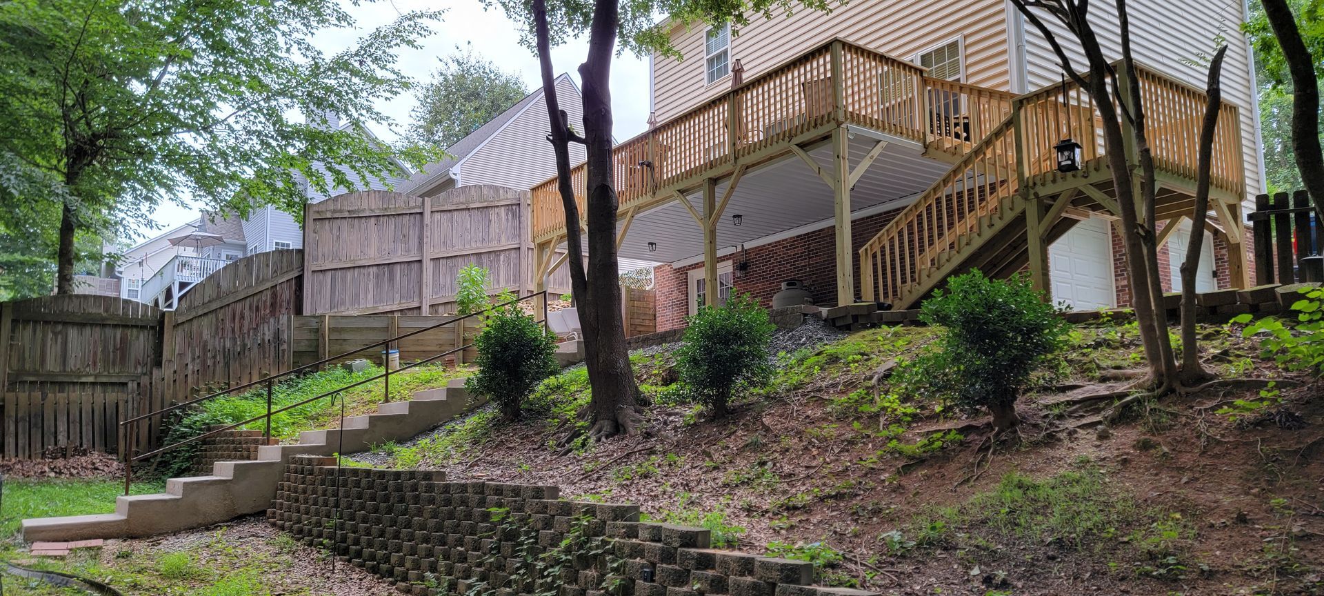 A large wooden deck is sitting on top of a hill next to a house.