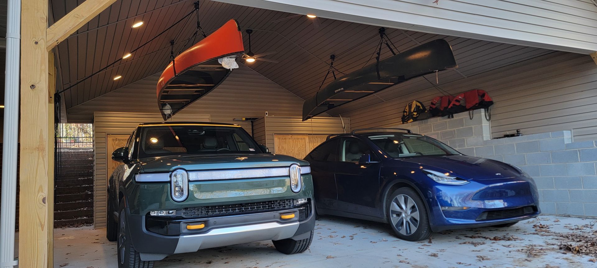 Two cars are parked in a garage with a canoe hanging from the ceiling.