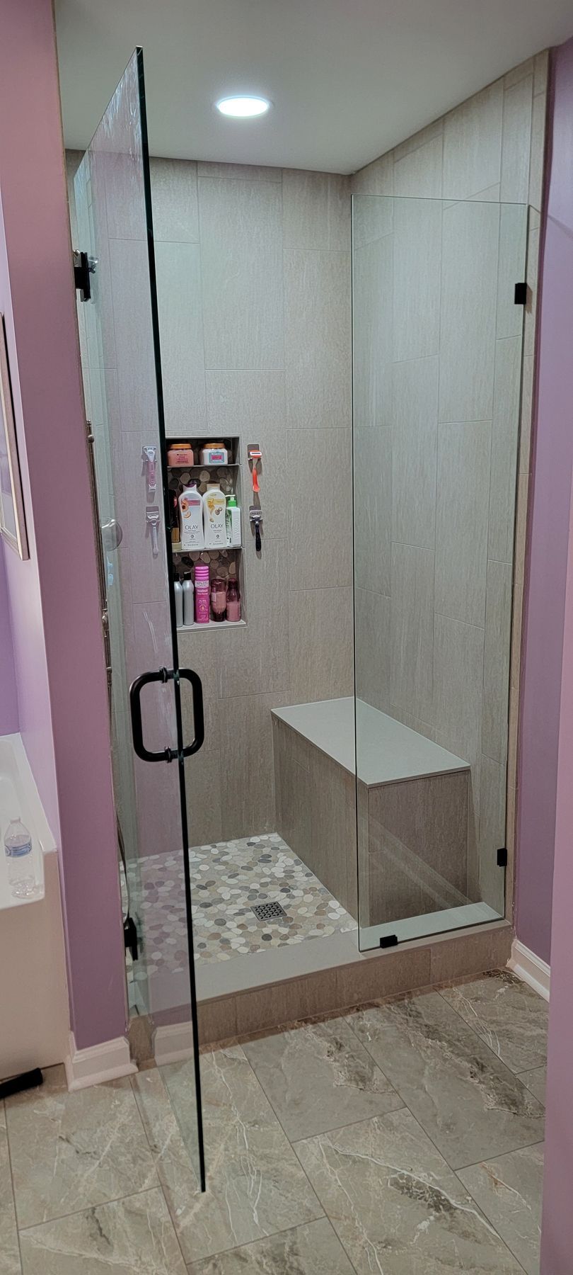 A bathroom with a walk in shower with a bench and a glass door.