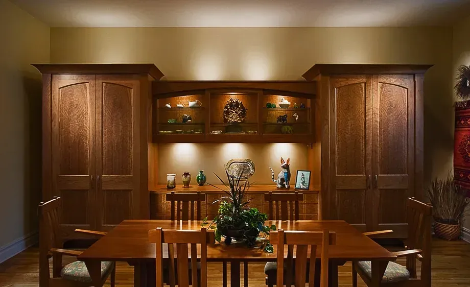 Dining room with a wood dining table, chairs, and built-in cabinets with display shelves illuminated by spotlights.