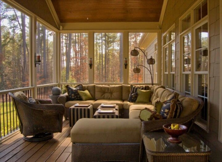A cozy screened porch with a sectional sofa, wicker chair, and view of trees. Soft lighting and neutral tones create a relaxing atmosphere.