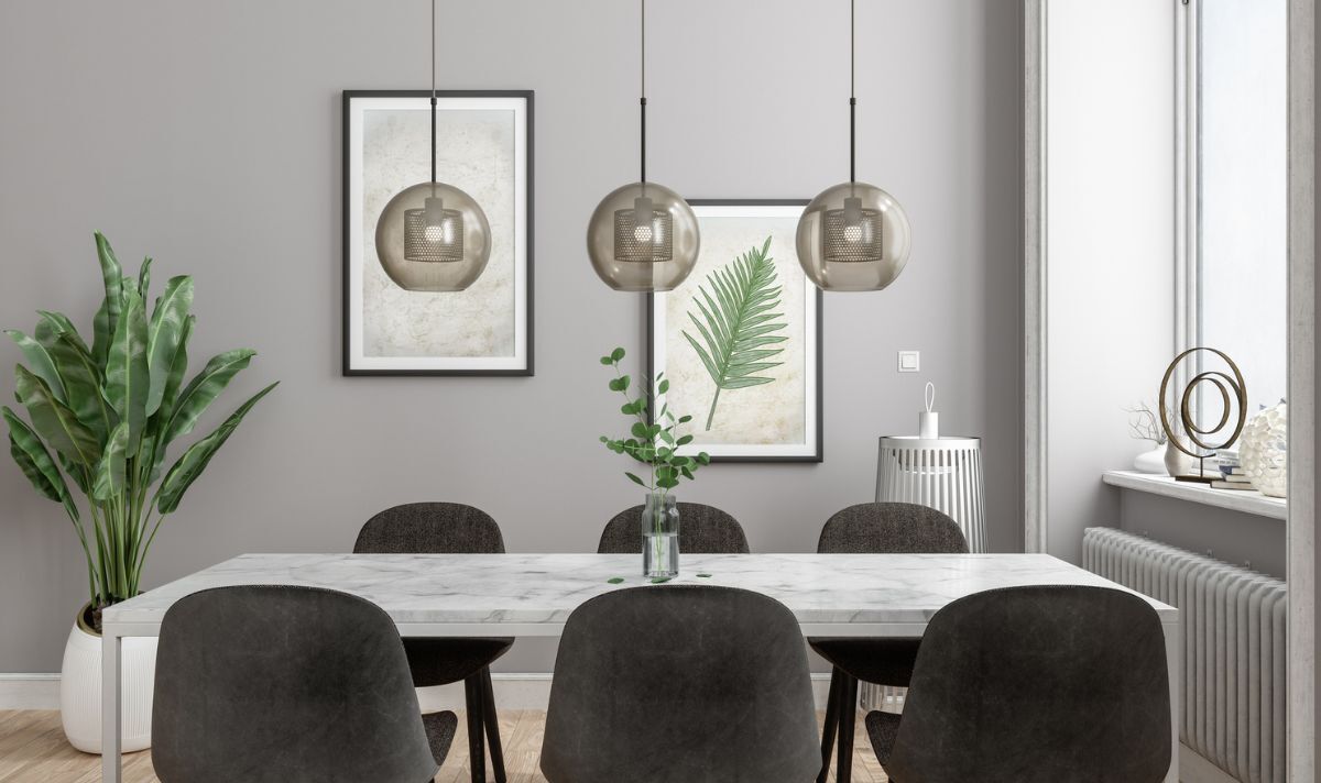 Dining room with gray walls, a white table, dark chairs, three hanging globe lights, and botanical art. A snake plant and vase of greenery decorate the table.