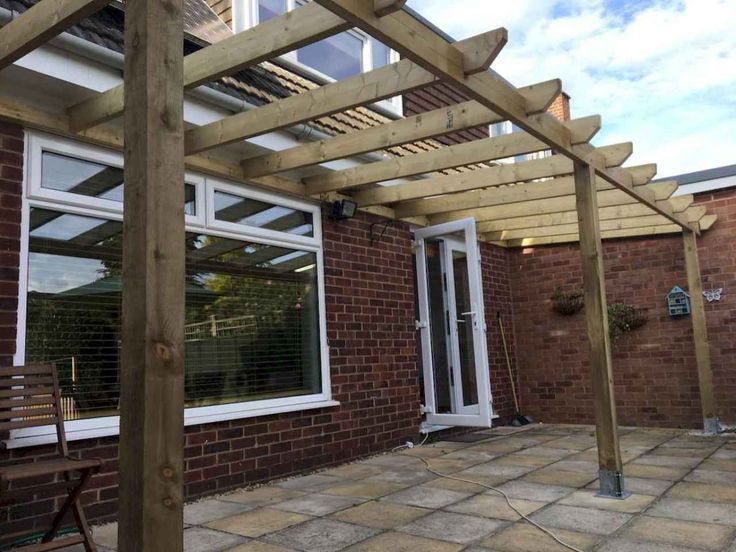 A wooden pergola is sitting on top of a patio in front of a brick house.