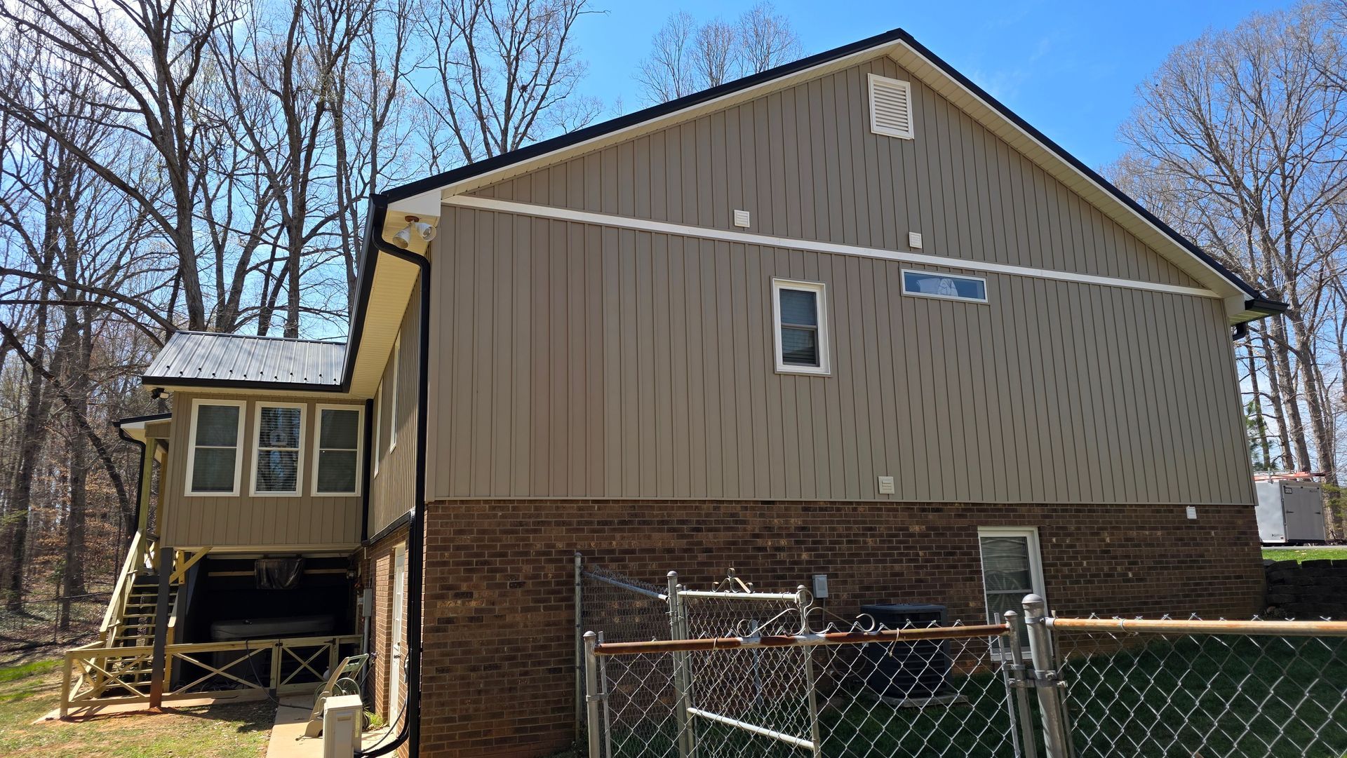The back of a house with a fence and trees in the background.